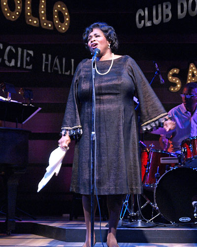 a woman in a black dress singing on stage